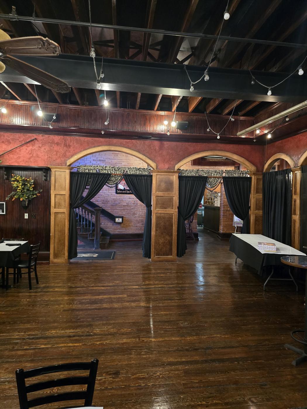 The dining room: exposed timber roof, red plaster walls, three brick archways hung with black drapes, and a dark polished wood floor.